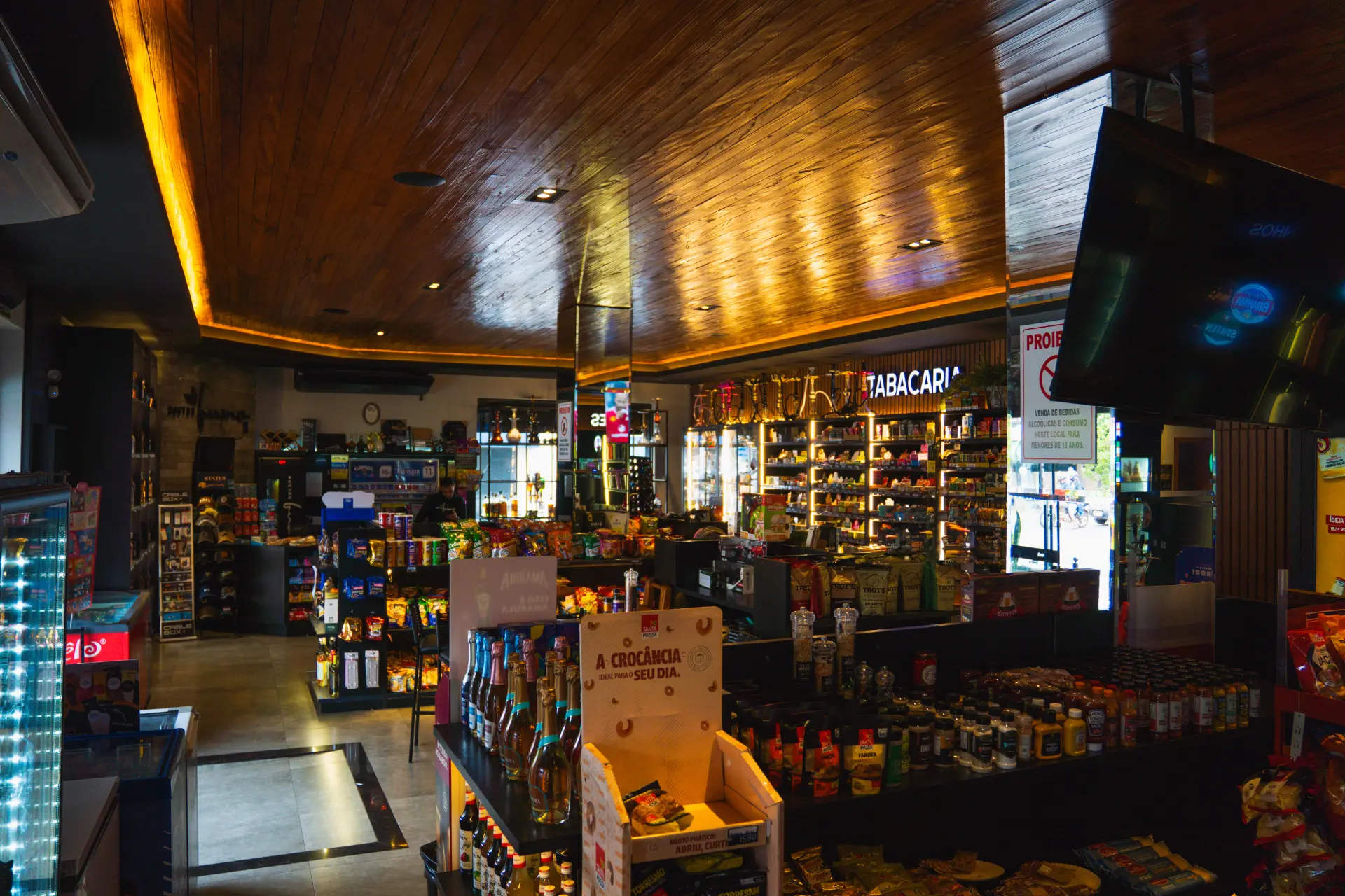 Interior da Nostro Ibiporã com teto de madeira iluminado, tabacaria e corredores de produtos